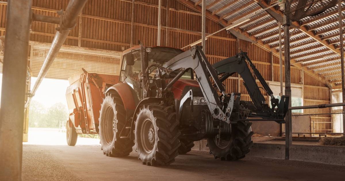 Un tractor modern roșu și negru, echipat cu încărcător, parcat într-un hambar spațios din lemn