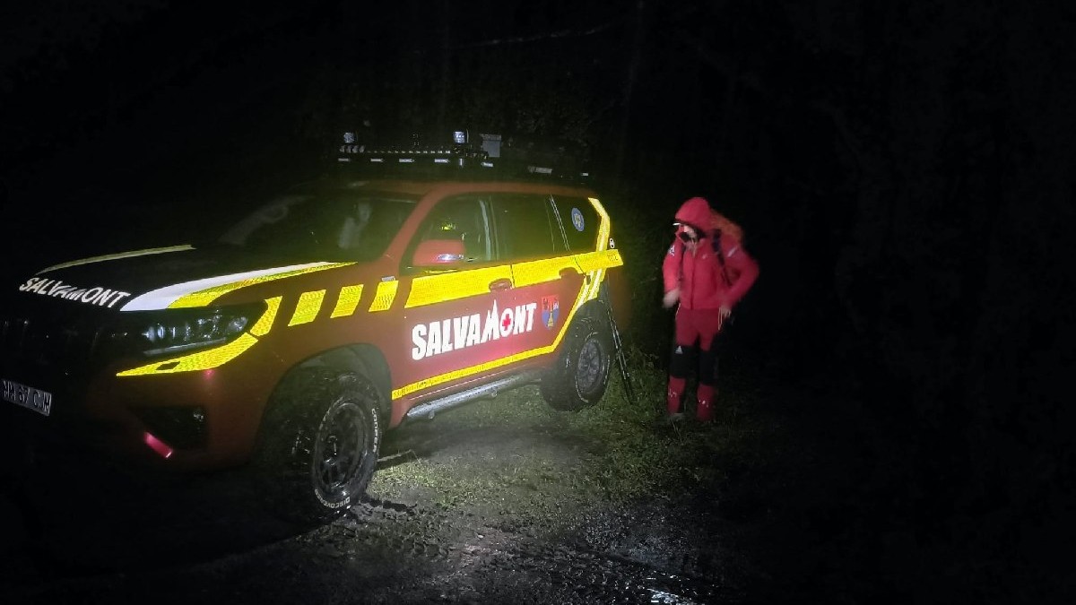 O mașină roșie, pe care scrie salvamont, lângă care este un salvamontist, fotografiată noaptea