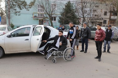 Victor Nicolae se deplasează în scaun rulant, după ce oamenii lui ”Bușcă” i-au tăiat piciorul stâng. Părinții, în plan îndepărtat, privesc cu durere spre fiul lor FOTO: Sorin Cioponea