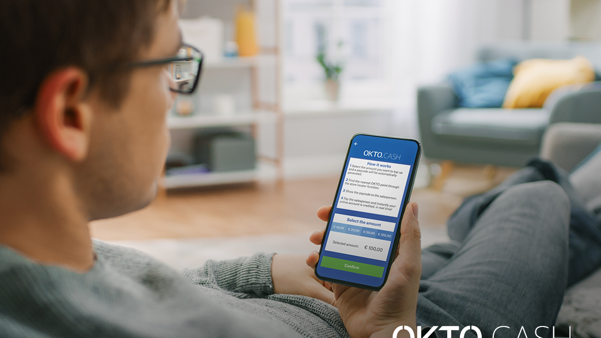 okto cash - barbat cu ochelari, asezat pe canapea in sufragerie, stand cu telefonul in mana, verificandu-si aplicatia okto