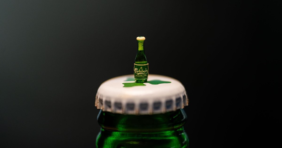 O mini sticlă de bere Carlsberg, pusă pe capacul unei sticle normale de bere