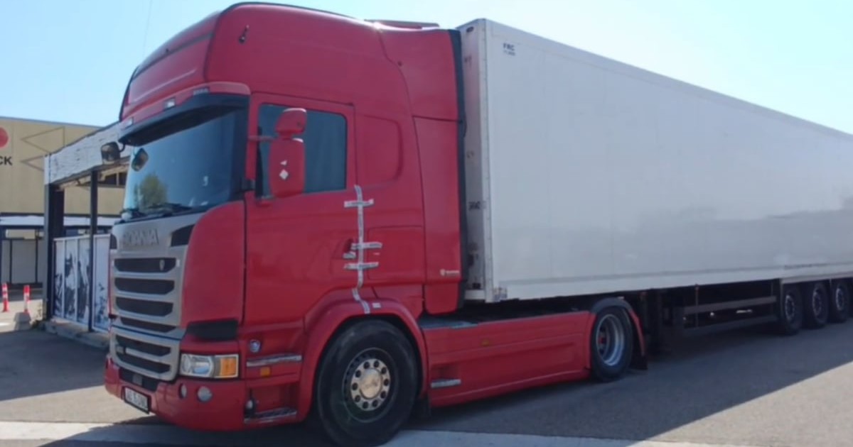 Un camion cu cabină roșie și remorca albă într-o parcare.