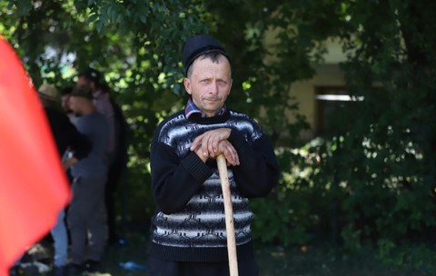 Ciobanul Liviu din Bihor, un bărbat cu un pulover albastru de lână, lângă un gard viu din București. Își ține capul sprijinit într-un toiag