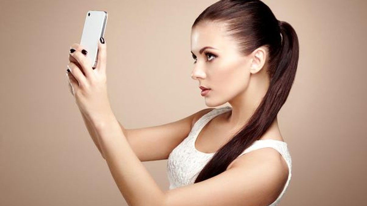 Telefonul mobil, principala cauză de gelozie la români. Fată brunetă făcându-și selfie