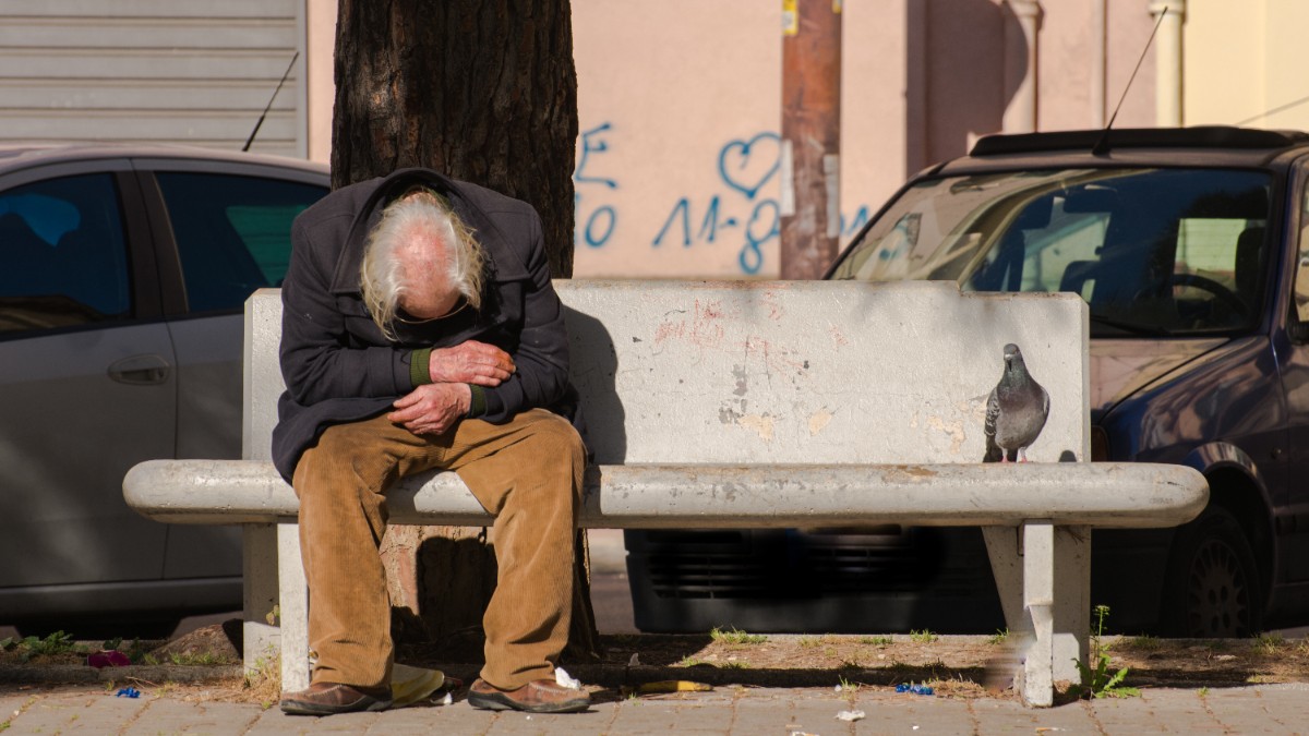 Un bărbat în vârstă care stă pe bancă, cu capul în jos