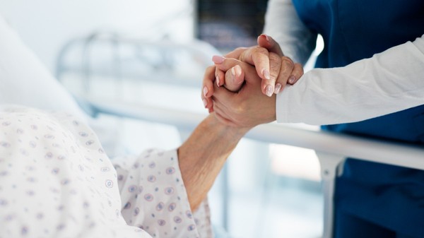 O persoană care ține mâna unei femei aflate pe un pat de spital