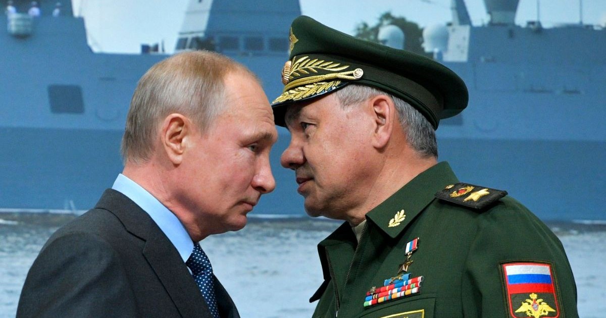 Vladimir Putin (stânga), îmbrăcat într-un sacou bleumarin și o cămașă bleu, și ministrul rus al Apărării, Serghei Șoigu (dreapta), îmbrăcat într-o uniformă militară navală de ceremonie, de culoare verde închis, în timpul unei vizite la un șantier naval din Sankt Petersburg aprilie 2019