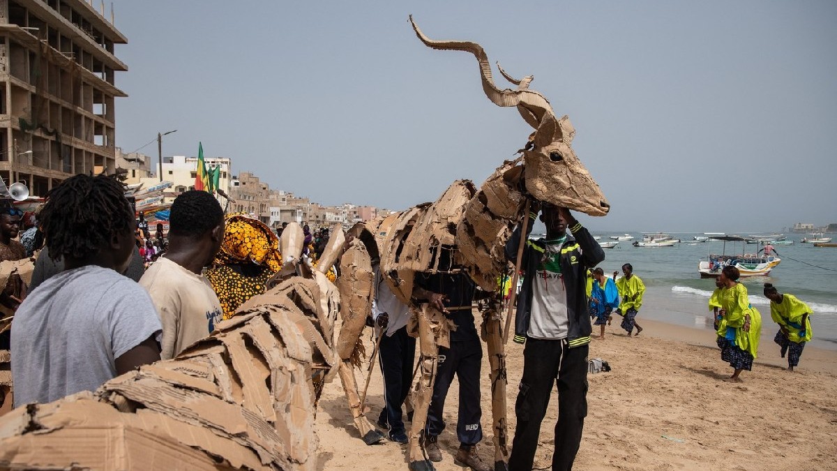 Un păpușar stă lângă păpuși de animale în mărime naturală, parte a proiectului de artă publică și acțiune climatică Herds, pe plaja Ngor din Dakar, la 26 aprilie 2025.
