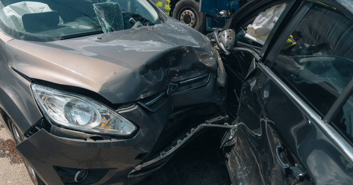 Fotografie în urma unui accident între două mașini. Una de culoare gri, iar cealaltă de culoare neagră. Cea are portiera laterală complet distrusă