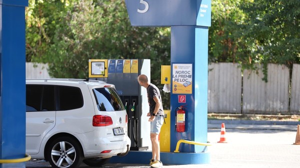 Un bărbat care se uită la ecranul unei pompe dintr-o stație de carburanți, lângă un autoturism alb Volkswagen parcat pentru alimentare. Foto: Libertatea/ Dumitru Angelescu
