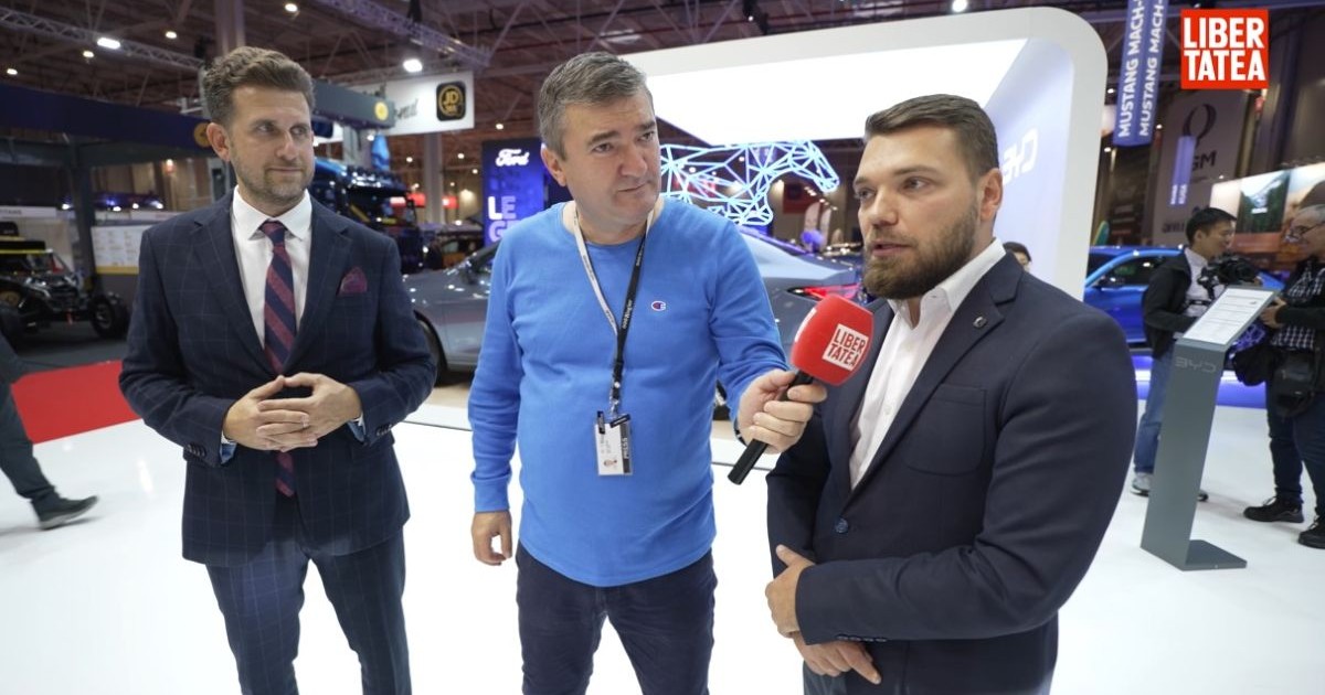 Andrei Duică, în stânga, îmbrăcat în costum, Dorin Chioțea, la mijloc, îmbrăcat cu o bluză albastră, în timp ce ține microfonul Libertatea către Andrei Pană, în dreapta, îmbrăcat în costum, la standul BYD de la Salonul Auto București 2025