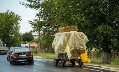 O căruță încărcată cu fân este depășită de un automobil de lux în Deveselu
