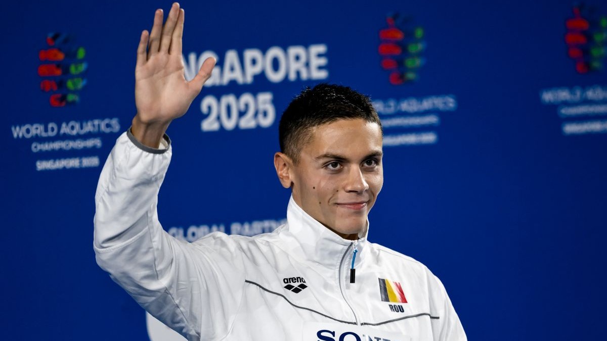 David Popovici salută publicul cu mâna dreaptă pe podiumul de premiere de la CM din Singapore, după ce a obținut medalia de aur în proba de 100 metri liber, iulie 2025