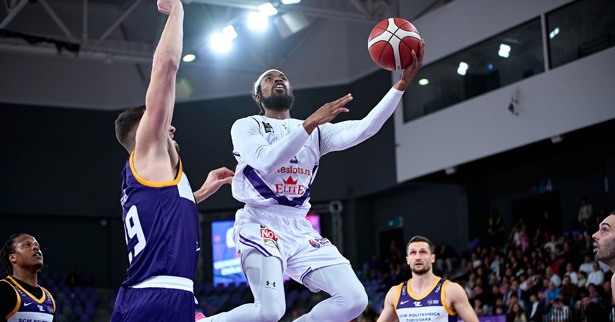 Un basketbalist de culoare imbracat in alb aruncă la cos o minge rosie