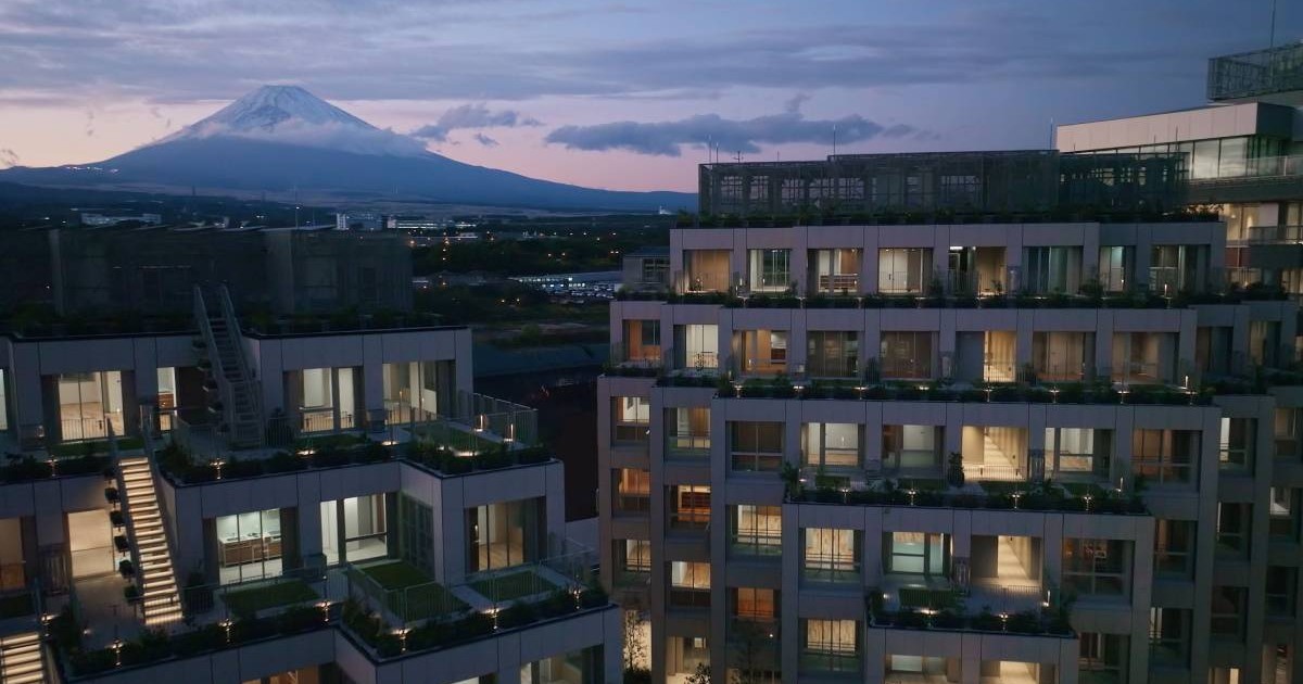 O randare cu orașul viitorului din Japonia, blocurile sunt înalte, apartamentele au luminile aprinse și scări interioare.