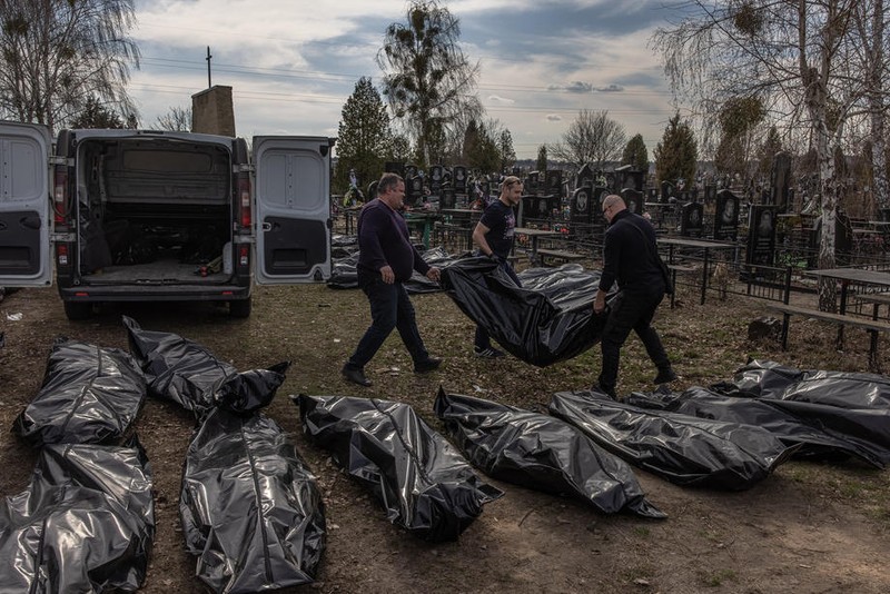 Voluntari cară trupurile găsite într-o groapă comună din Bucha, după plecarea forțelor ruse | Foto: EPA