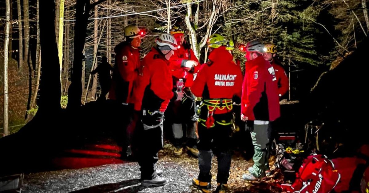 O echipă de șase salvamontiști, cu haine roșii și caschete, sunt în pădure și caută un turist rătăcit și epuizat, care a cerut ajutorul, 23 noiembrie 2025