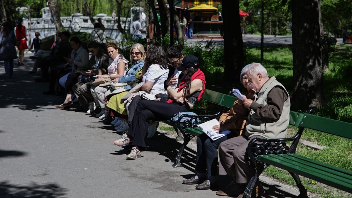 Mai mulți pensionari stau pe o bancă în parcul Cișmigiu din București
