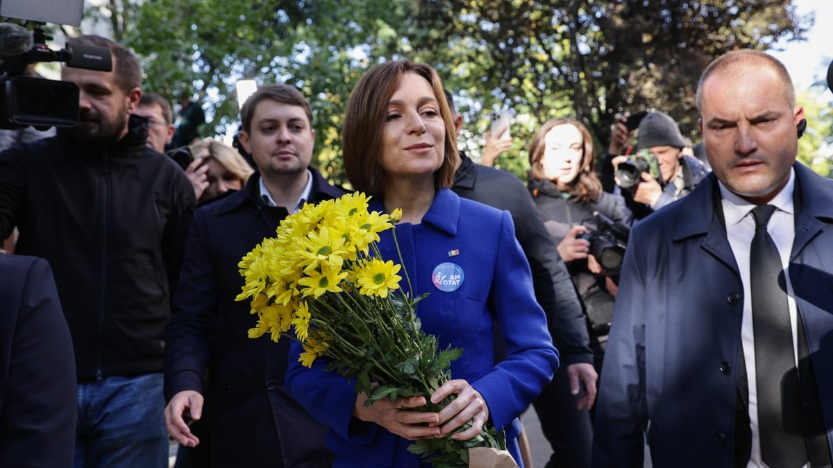 maia sandu, in costul albastru, tine un buchet de flori galbena in mana si este inconjurata de mai multi oameni