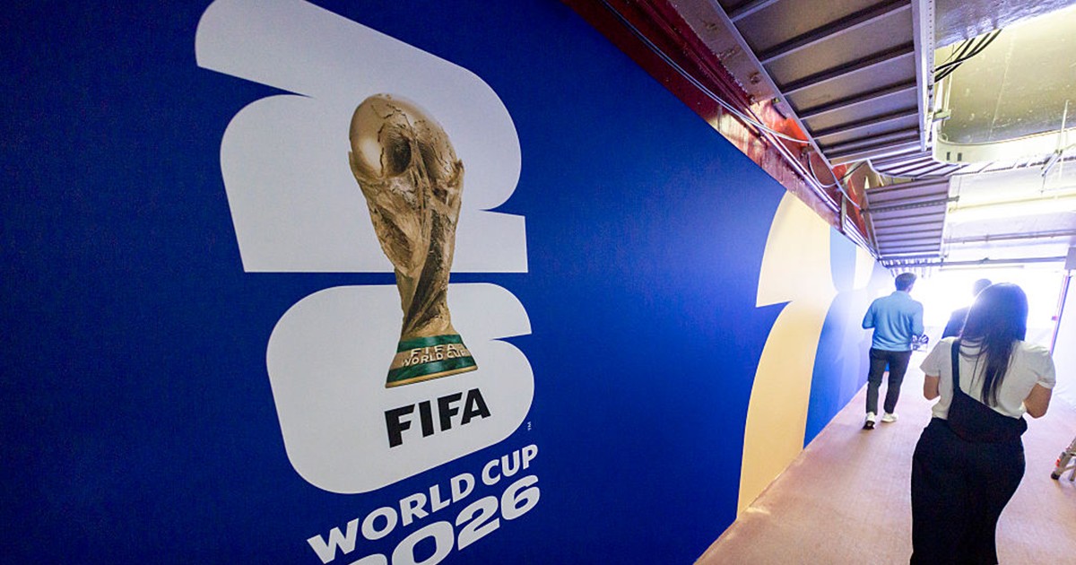 Un afiș pe care scrie FIFA 2026 și pe lângă care trec persoane.