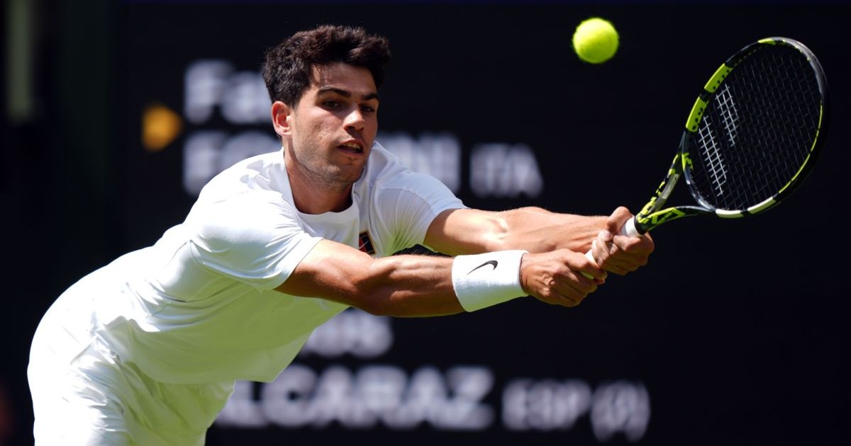 Carlos Alcaraz, îmbrăcat în alb, se întinde și returnează o minge în timpul unei partide de la Wimbledon, iunie 2025