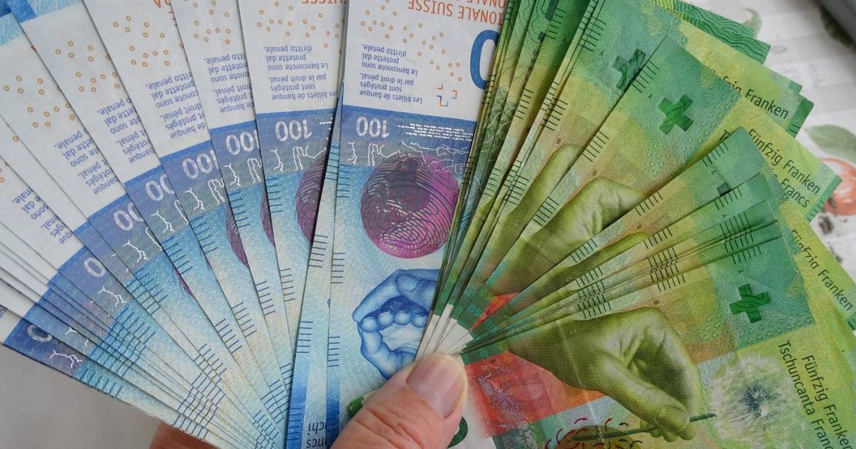 O femeie ține în mână mai multe bancnote de 50 și de 100 de franci elvețieni
