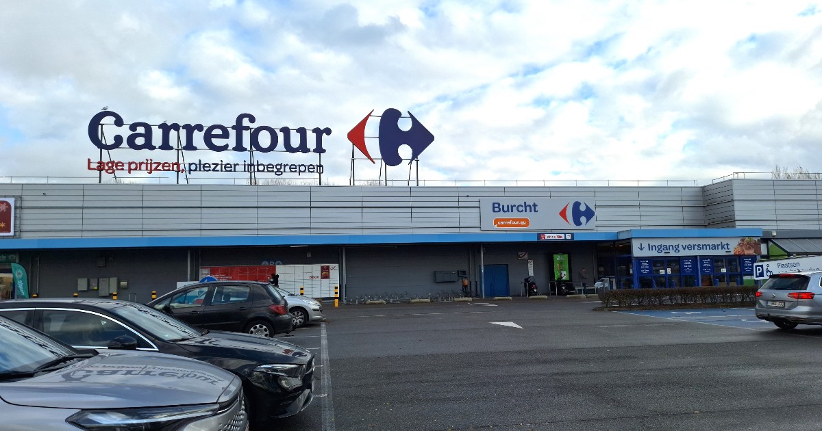 Imaginea surprinde exteriorul unui hipermarket Carrefour, cu logo-ul vizibil pe clădire și o parcare largă în prim-plan, unde sunt parcate mai multe autoturisme. Clădirea are o fațadă modernă, iar intrarea principală este semnalizată clar, sub un cer parțial noros.