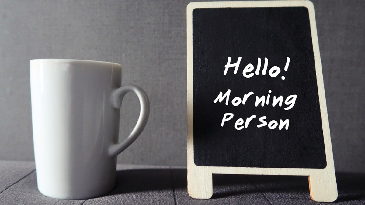Ce sunt cronotipurile şi cum afectează somnul - Imagine cu o cană albă de cafea alături de o tăbliţă pe care scrie "Hello! Morning Person".
