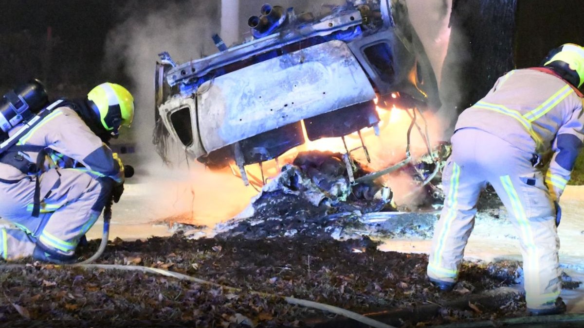 În prim-plan este o mașină întoarsă pe capotă și arsă, flăcări încă se mai văd, iar în stânga și dreapta sunt doi polițiști care se uită la ea, decembrie 2025, Haga