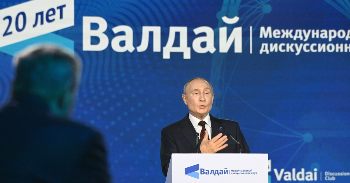 Președintele rus Vladimir Putin luând cuvântul la pupitru în cadrul ședinței a celei de-a XXI-a reuniuni anuale a clubului internațional de discuții „Valdai”. Putin este imbracat intr-un costum negru, camasa alba si cravta, iar in spatele lui se observa un panou urias cu numele clubului Valdai