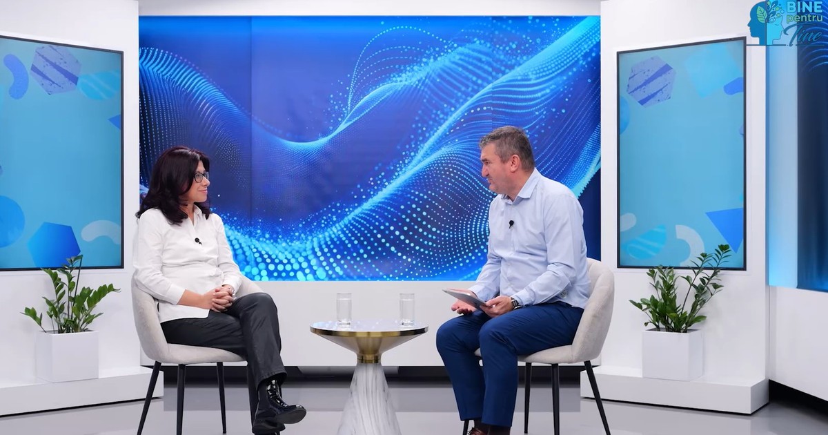 Viorica Elena Rădoi (stanga), medic genetician și Șefa Departamentului de Genetică la Spitalul Clinic Sanador, a fost invitata lui Dorin Chioțea (dreapta) în emisiunea „Bine pentru tine”. Viorica Elena Rădoi este imbracata in pantaloni negri si camasa alba, iar Dorin Chiotea in blugi albastri si camasa albastra. cei doi stau pe scaune in jurul unei mese si in spate se observa un fundal al albastru specific culorilor emisiunii