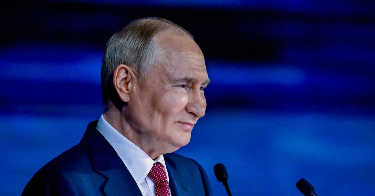 Vladimir Putin a fost surprins zâmbind la Forumul Economic de la Sankt Petersburg, desfășurat în iunie 2025. Liderul rus poartă un sacou albastru, o cravată roșie și o cămașă albă și se află în fața unui microfon