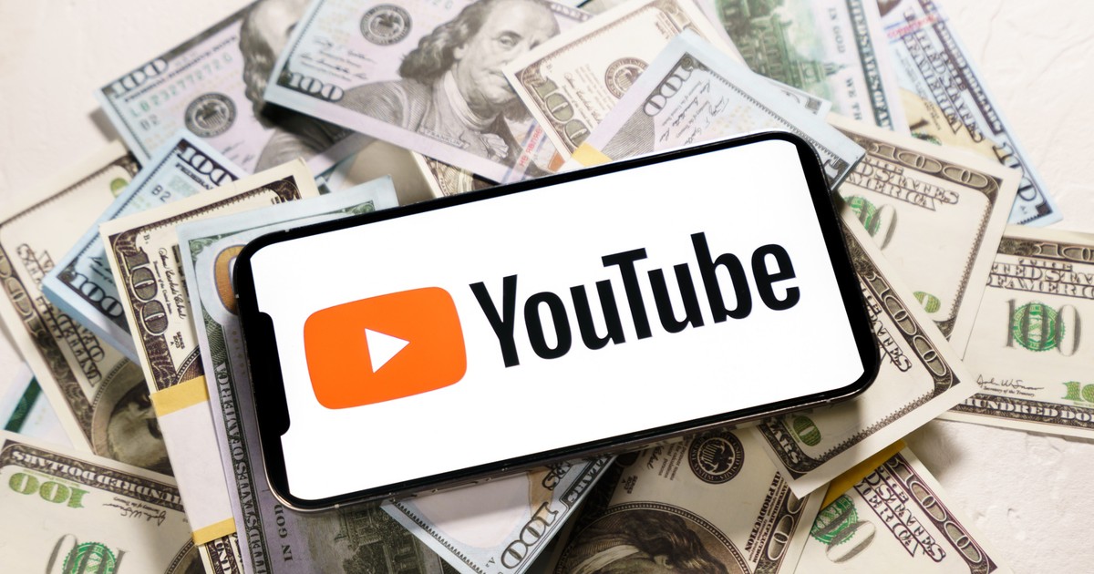 Cum poţi să câștigi bani pe YouTube - Imagine cu un telefon ce are pe ecran sigla YouTube şi este aşezat pe un teanc de bani
