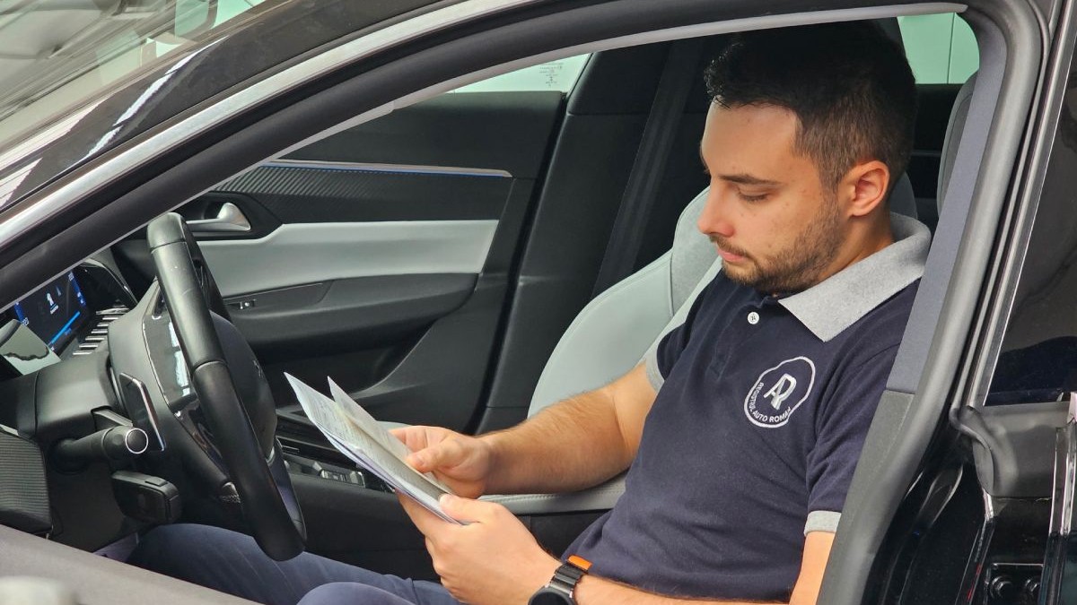 Un inginer RAR, îmbrăcat cu un tricou care are sigla RAR, în interiorul unei mașini, cu documente în mână