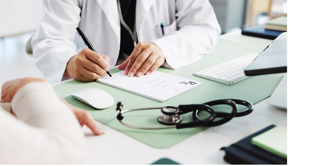 Un medic imbracat in halat alb sta la birou si scrie. Prima zi de concediu medical e și neplătită, și tăiată din vechimea la pensie. Foto Shutterstock