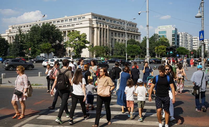 Bucharest, Romania - July 14, 2021: People cross the street near the Victoria Palace which houses the Romanian Government headquarters, in Bucharest.