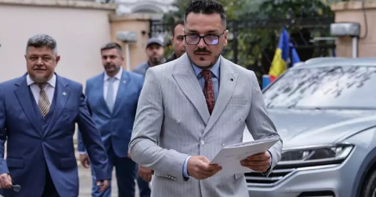 Influencerul Alexandru Virgil Zidaru, cunoscut publicului drept Makaveli, îmbrăcat în costum și ținând în mână un dosar