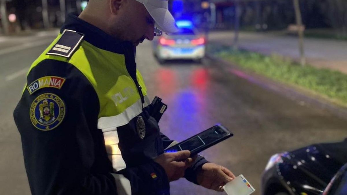 Polițist de la Rutieră, îmbrăcat în uniformă, în timp ce verifică buletinul unui șofer oprit în trafic