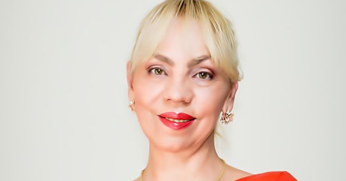Ioana Scoruș îmbrăcată într-o bluză roșie, cu buze roșii și părul prins zîmbește către cameră.