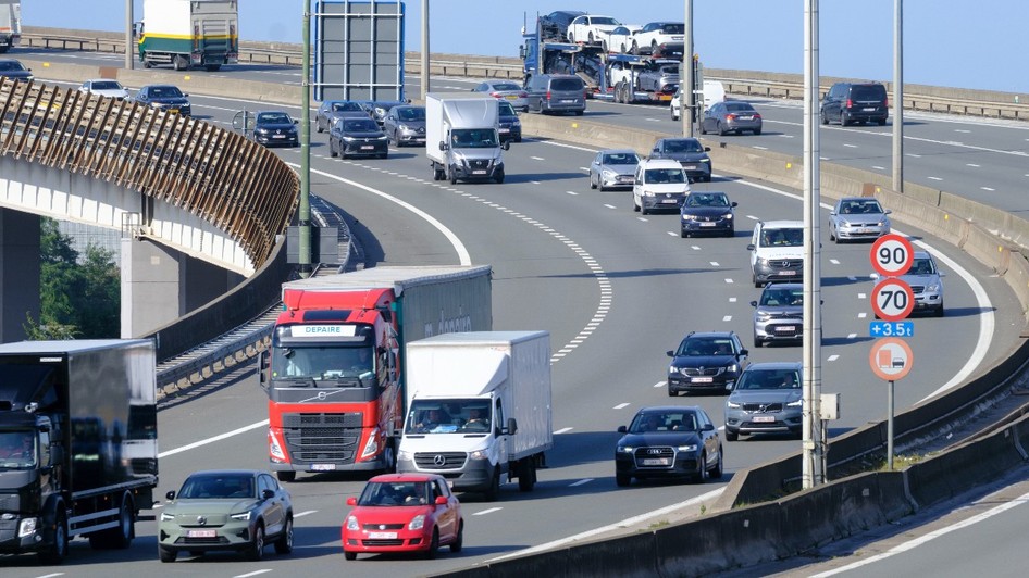 Trafic intens de autoturisme, camionete și camioane în deplasare pe un nod rutier supraetajat al unei autostrăzi.
