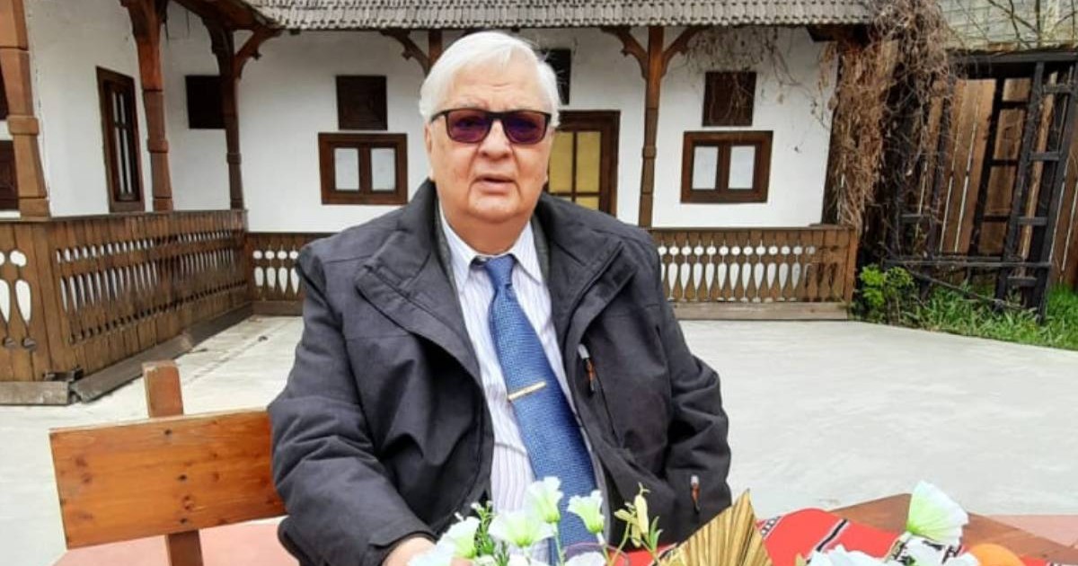 Mircea Coșea, profesor, economist, fost viceprim-ministru al României, asezat pe o banca, in aer liber, in fata lui pe masa niste flori , in spate se vede o casa cu pereti albi si lemn. Mircea Cosea a murit joi, 18 decembrie 2025