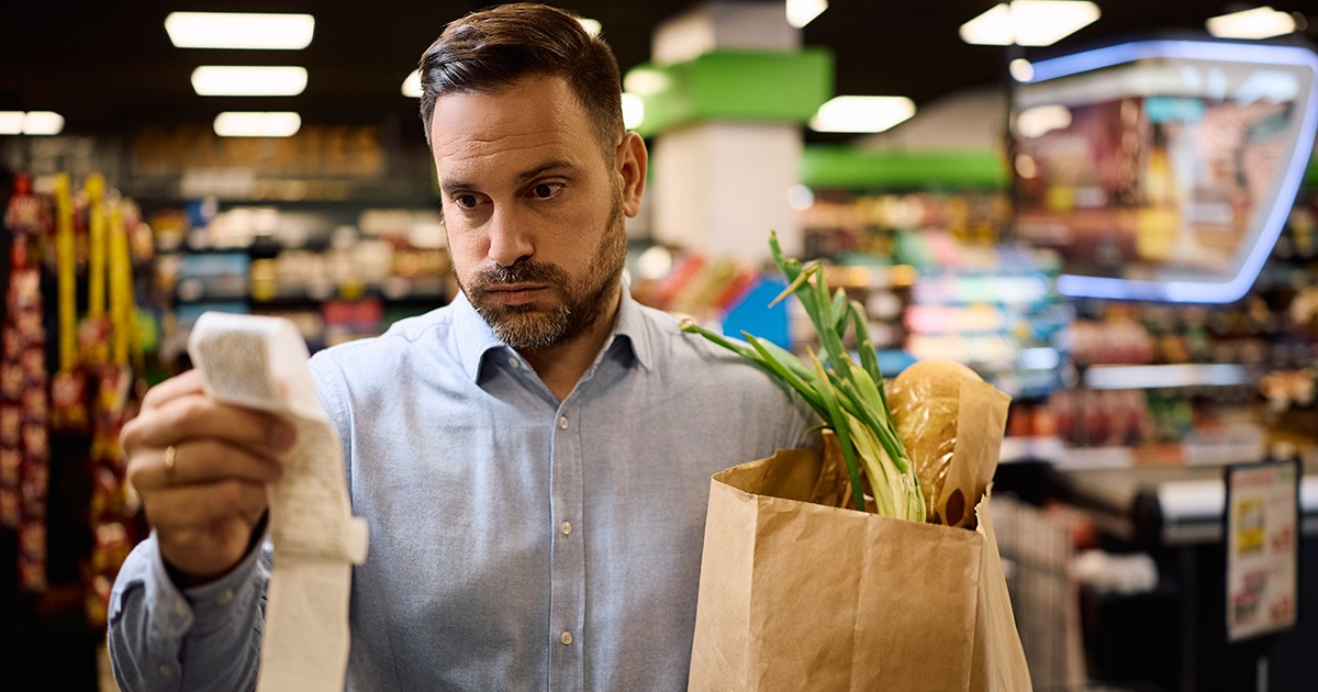 Omul îngrijorat verifică factura după ce cumpără alimente la supermarket