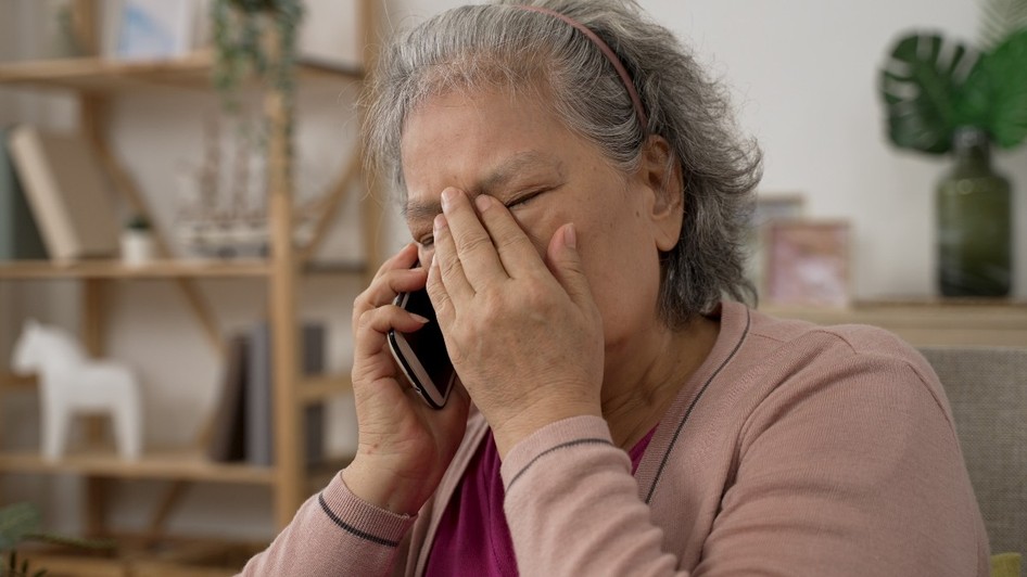 O femeie bătrână care vorbește la telefon și ține o mână pe frunte