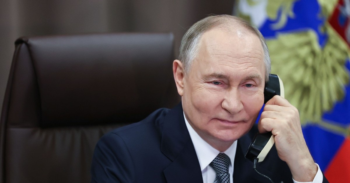 Vladimir Putin vorbește la un telefon fix, în spate, dreapta, steagul Rusiei