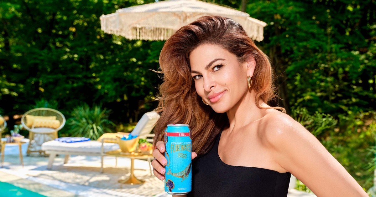 Eva Mendes la psicina intr-un costul de baie intreg negru decupat pe un umar, tine in mana o doza albastru turqoise de Floe Water
