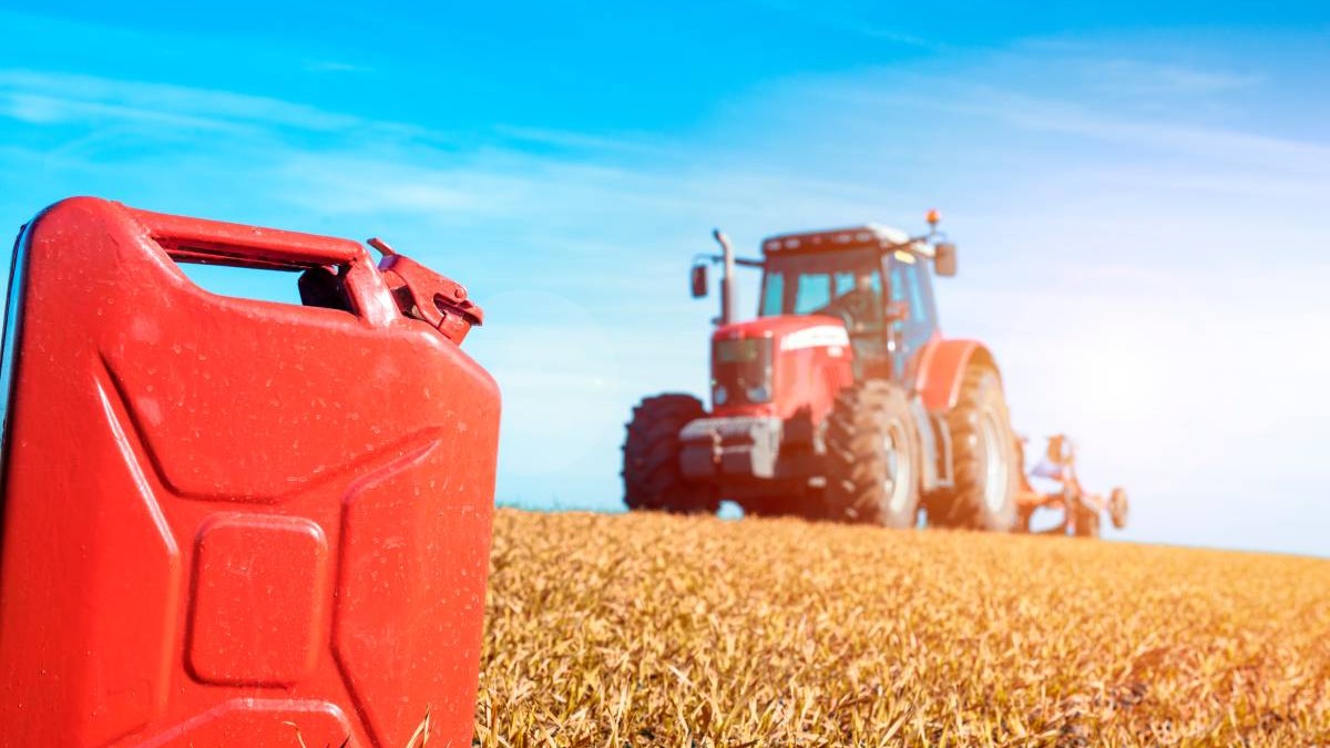 Tractor pe camp in soare, in prim plan o canistră de combustibil. Comceptul de motorina scumpa