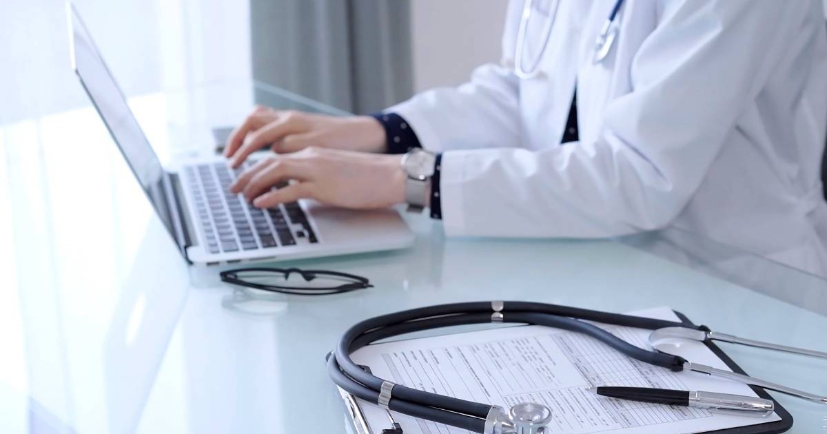 medic care tasteaza la computer, pe masa are foi si un stetoscop