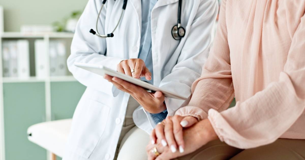Un medic și o pacientă în timpul consolației, datele sunt digitalizate și pot fi verificate pe o tabletă pe care medicul îi arată ceva femeii.