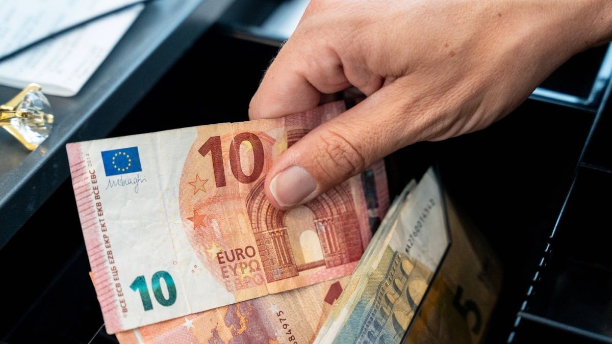 O mână scoate numerar dintr-o casă de marcat deschisă sau dintr-un sertar de numerar într-un magazin plin cu bancnote de 10 euro, 20 de euro și 5 euro, Germania, 3 iulie 2026