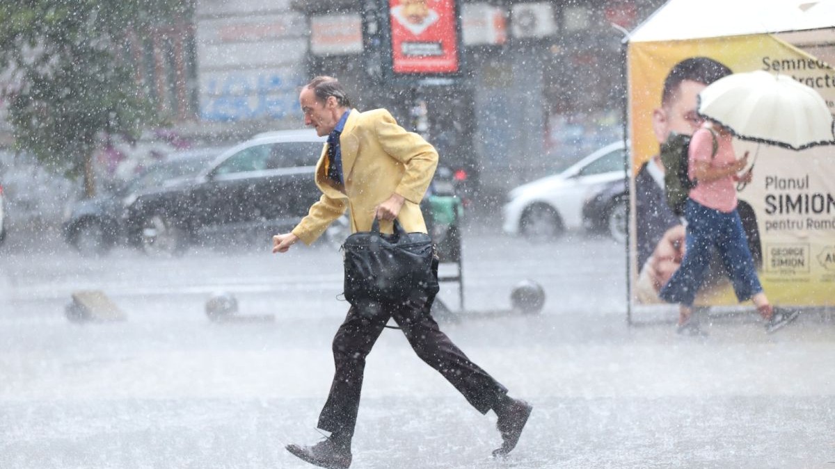Un bărbat îmbrăcat la sacou galben fuge printr-o ploaie abundentă, iar o femeie merge în direcția opusă, având o umbrelă în mână, în București